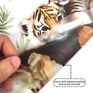 Detail showing hand peeling the adhesive backing of a cartoon tiger and leaves wall sticker