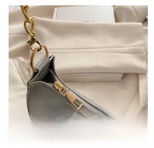 Detailed close-up of smooth gold metal zipper and leather texture on a grey shoulder bag