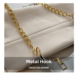 Close-up of golden metal chain, D-ring buckle and zipper on grey crescent handbag