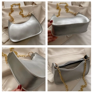 Detail view of a metallic silver crescent bag with chunky gold chain strap and mirror finish