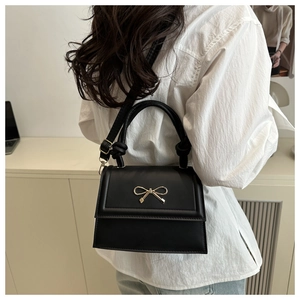 Detail of minimalist black leather crossbody bag with elegant golden bow buckle