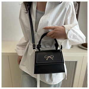 Detail of black mini crossbody bag with golden bow hardware and leather top handle strap