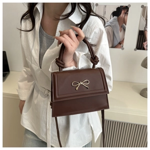 Detail of the brown faux leather handbag with golden bow accent and woven top handle strap