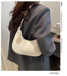 Detailed view of white woven texture hobo bag with a decorative gold M letter pendant