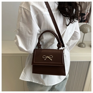 Detalle de bolso bandolera marrón oscuro con lazo dorado y asa con nudo elegante