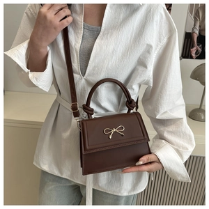 Bolso bandolera marrón con lazo dorado y asa superior anudada con diseño único