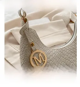 Detail of woven cream hobo bag with a gold M-shaped letter pendant and matte leather texture