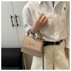 Detail of a beige mini square bag with metal bow accent and twisted handle on a model