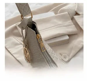 Detailed close-up of cream crocodile pattern bag with golden zipper and M charm