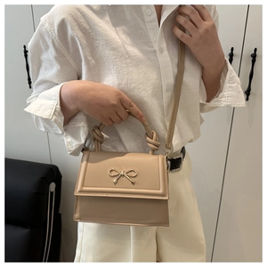 Detalle de bolso beige con lazo dorado y asa trenzada usado por una modelo