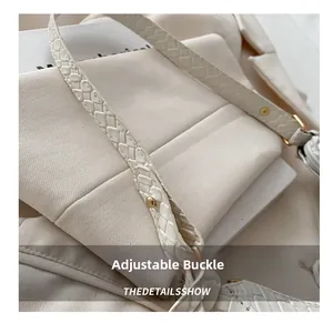 Close-up of woven shoulder strap on white handbag with gold buckle and rivets