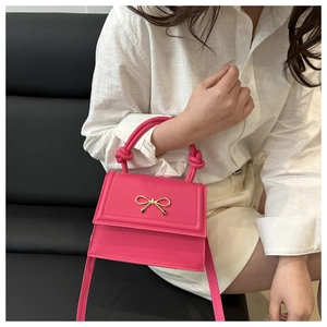 Detail of rose pink handbag featuring a knotted handle and golden bow decoration