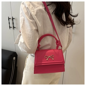 Bolso bandolera rosa fucsia con lazo dorado mostrado por una modelo en fondo blanco