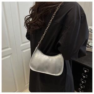 Close-up of a silver metallic hobo bag with a thick gold chain strap on a shoulder