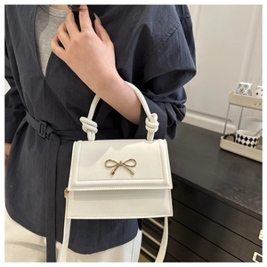 Detail of white leather crossbody bag with golden bow and knotted handle on model