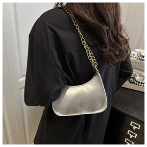 Detail of silver crescent bag with gold chain strap worn as a shoulder bag