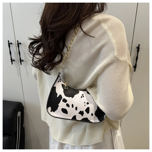 Detail shot of a cow print crescent bag with gold chain strap on a model shoulder