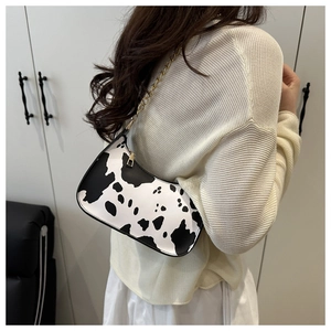 Detailed view of the cow print underarm bag with gold chain strap worn by a model