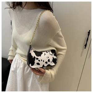 Detail of cow print shoulder bag featuring bold gold chain strap and glossy finish