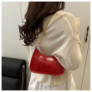 Detail of red semi-circle shoulder bag featuring glossy leather and gold chain strap