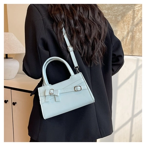 Detail of mint blue square bag with bow decoration worn over a black blazer