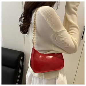 Detail of red patent leather shoulder bag featuring a sleek gold chain strap on model