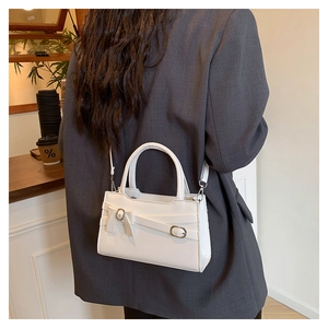 White mini square shoulder bag with bow detail worn by a model in a modern cafe setting