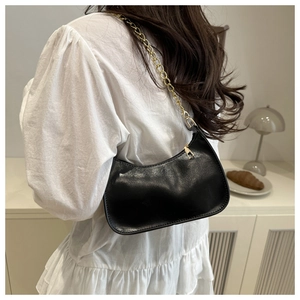 Detail of black crescent shoulder bag with glossy finish and gold chain strap