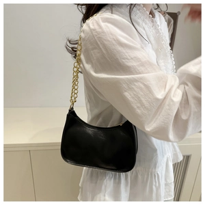 Detail shot of a black leather underarm bag with gold chain strap on a model