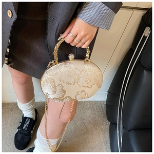 Detail of floral embroidery and gold round handle on cream brocade evening clutch bag