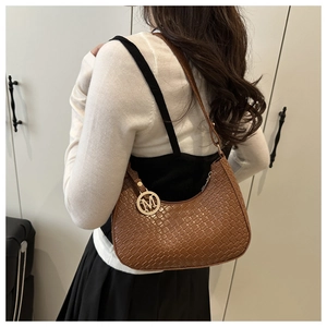 Detail of a brown woven hobo bag with a gold metal M charm worn by a model
