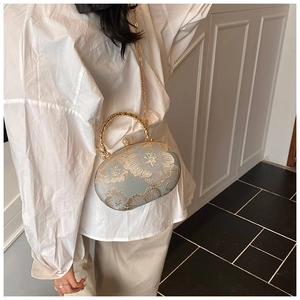 Detail of light blue satin evening bag with golden floral embroidery and metal ring handle