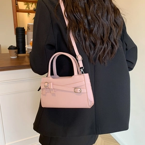 Stylish pink leather crossbody handbag with bow decoration worn by a model in a cafe