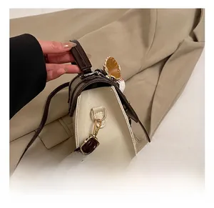Close-up of gold metal hook and strap detailing on cream faux leather crossbody bag