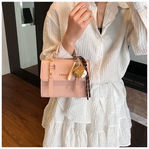 Detail of pink faux leather square crossbody bag with baseball tassel charm and gold rivets