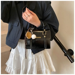 Detalle del bolso bandolera de charol negro con colgante de béisbol y herrajes dorados