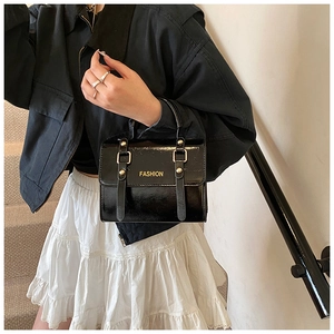 Detail of black patent leather messenger bag with gold fashion letters and hardware