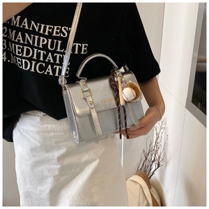 Detail of silver metallic crossbody bag with textured leather and baseball charm accessory