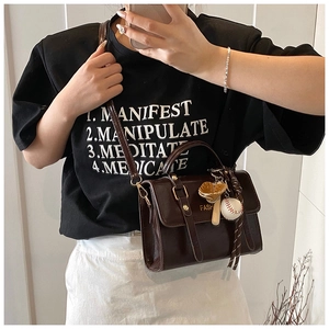 Detail view of brown messenger bag with baseball charm on model
