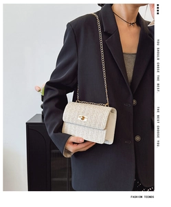 Close-up of white woven texture crossbody bag with gold metal lock and chain strap