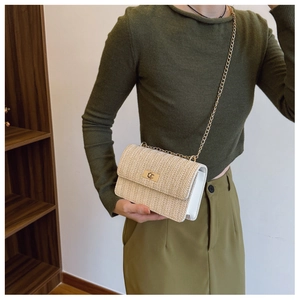 Detail of straw woven crossbody bag featuring a golden chain strap and stylish twist lock
