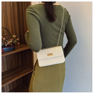 Detail of cream woven straw crossbody bag with golden chain and metallic turn-lock buckle