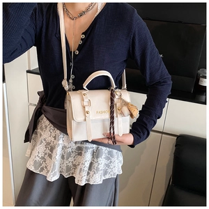 Detail of cream crossbody bag with gold FASHION text and a bear charm pendant