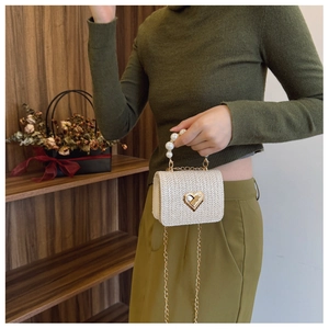 Detail view of woven beige crossbody bag with heart lock, pearl handle and gold chain