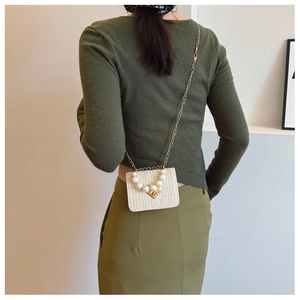 Detail of woven beige crossbody bag featuring large pearl trim and gold triangle clasp