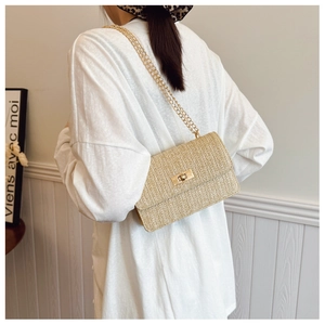 Detail of straw woven chain bag with V-shaped texture and gold metal lock on model