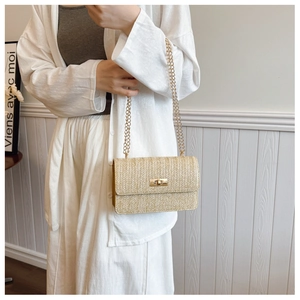 Close-up of beige woven texture bag with gold chain strap and metallic clasp on model