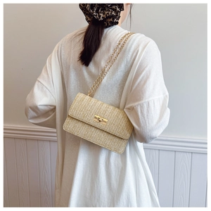 Detail of straw woven crossbody bag with gold chain strap and metal turn-lock closure