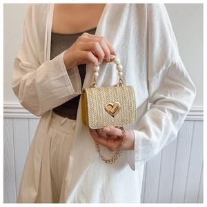 Detail of straw mini bag featuring a gold heart twist lock and pearl bead handle