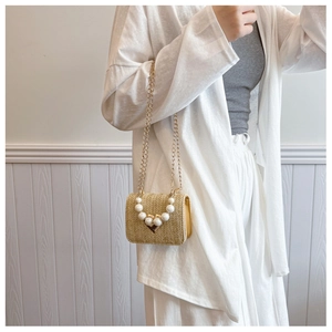 Detail of woven straw bag featuring pearl handle and golden heart clasp on white attire